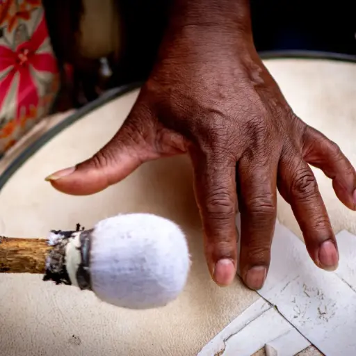 Mão negra sobre tambor enquanto baqueta se aproxima para batida durante apresentação musical.